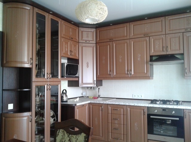 Klasyczna kuchnia na wymiar w odcieniach brązu, z frezowanymi frontami, szklanymi witrynami i subtelnym oświetleniem. Widoczny piekarnik i kuchenka gazowa.