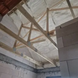 Poddasze z drewnianą konstrukcją pokryte białą pianą PUR, widok z dołu, fragment ściany z betonu komórkowego po prawej. Ocieplenie natryskowe.