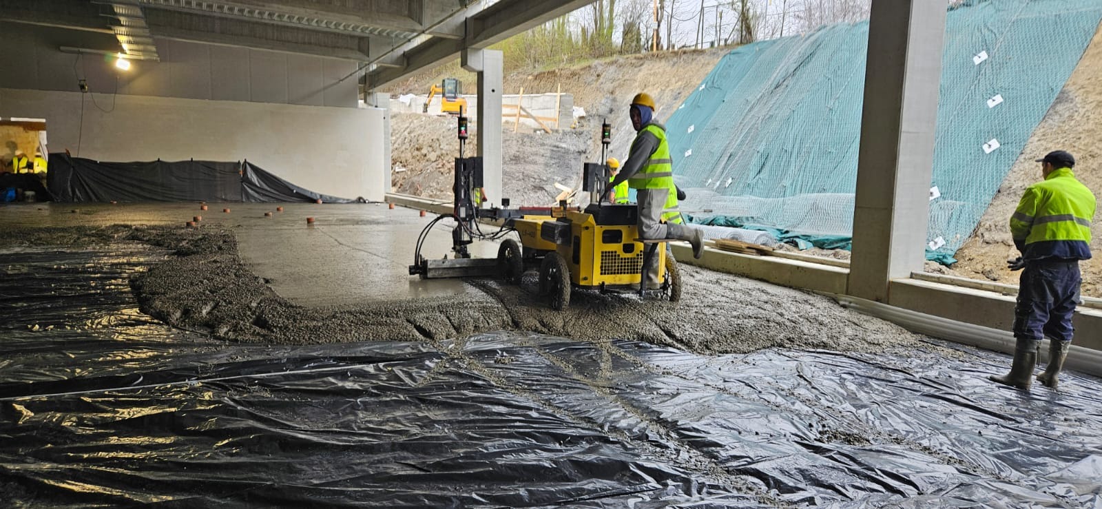 Wylewka posadzki przemysłowej w Boruja Kościelna wykonywana maszynowo z użyciem listwy wibracyjnej na folii. Widoczny pracownik w żółtej kamizelce.