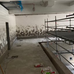 Spotless Yan Babkin - Wnętrze w trakcie prac: ułożone płytki na ścianach w mozaikę, worki z zaprawą na podłodze, rusztowania. Widoczne instalacje pod sufitem.