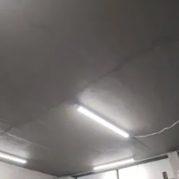 Szary sufit po szpachlowaniu i wygładzeniu z widocznymi liniami łączeń płyt i dwoma lampami jarzeniowymi, wykonany w garażu.