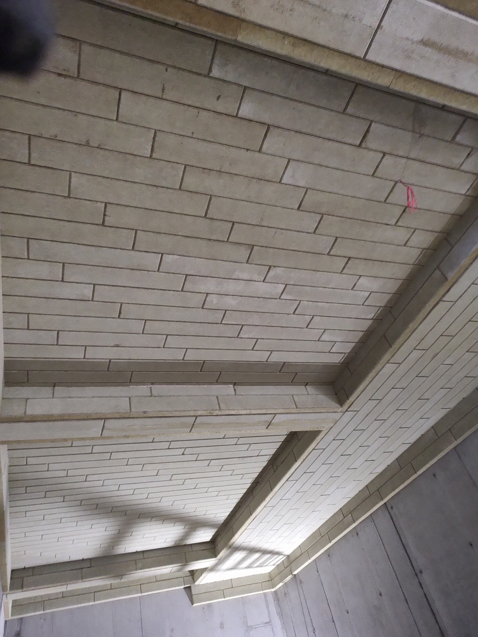 Ocieplony strop garażu podziemnego z widocznymi panelami izolacyjnymi ułożonymi w cegiełkę, z elementami konstrukcyjnymi. Szare ściany w tle.