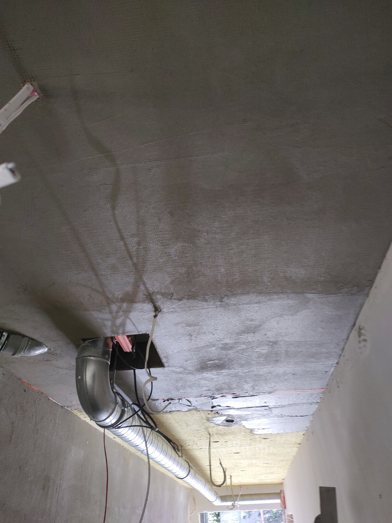 Sufit korytarza w trakcie ocieplania: wełna, siatka zatopiona w kleju, widoczne przewody wentylacyjne i instalacje. Przygotowanie do tynku dekoracyjnego lub gładzi.