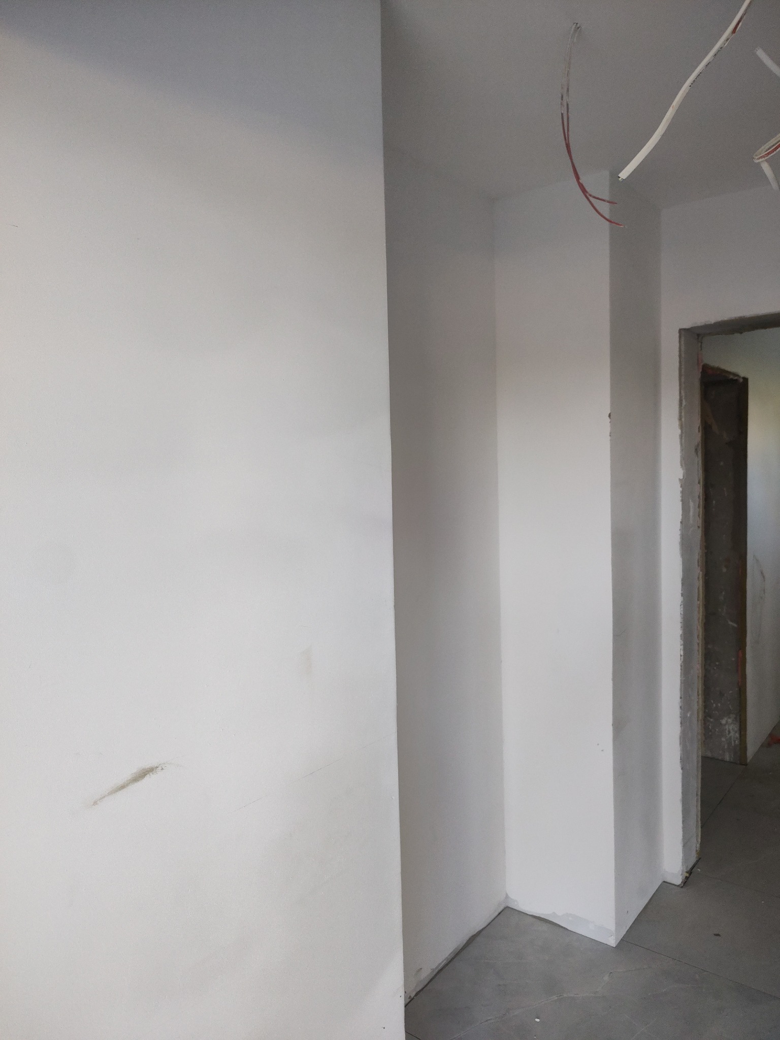 Korytarz po nałożeniu gładzi i pomalowaniu na biało w Krakowie. Widoczne wystające kable z sufitu i fragment ościeżnicy drzwi.