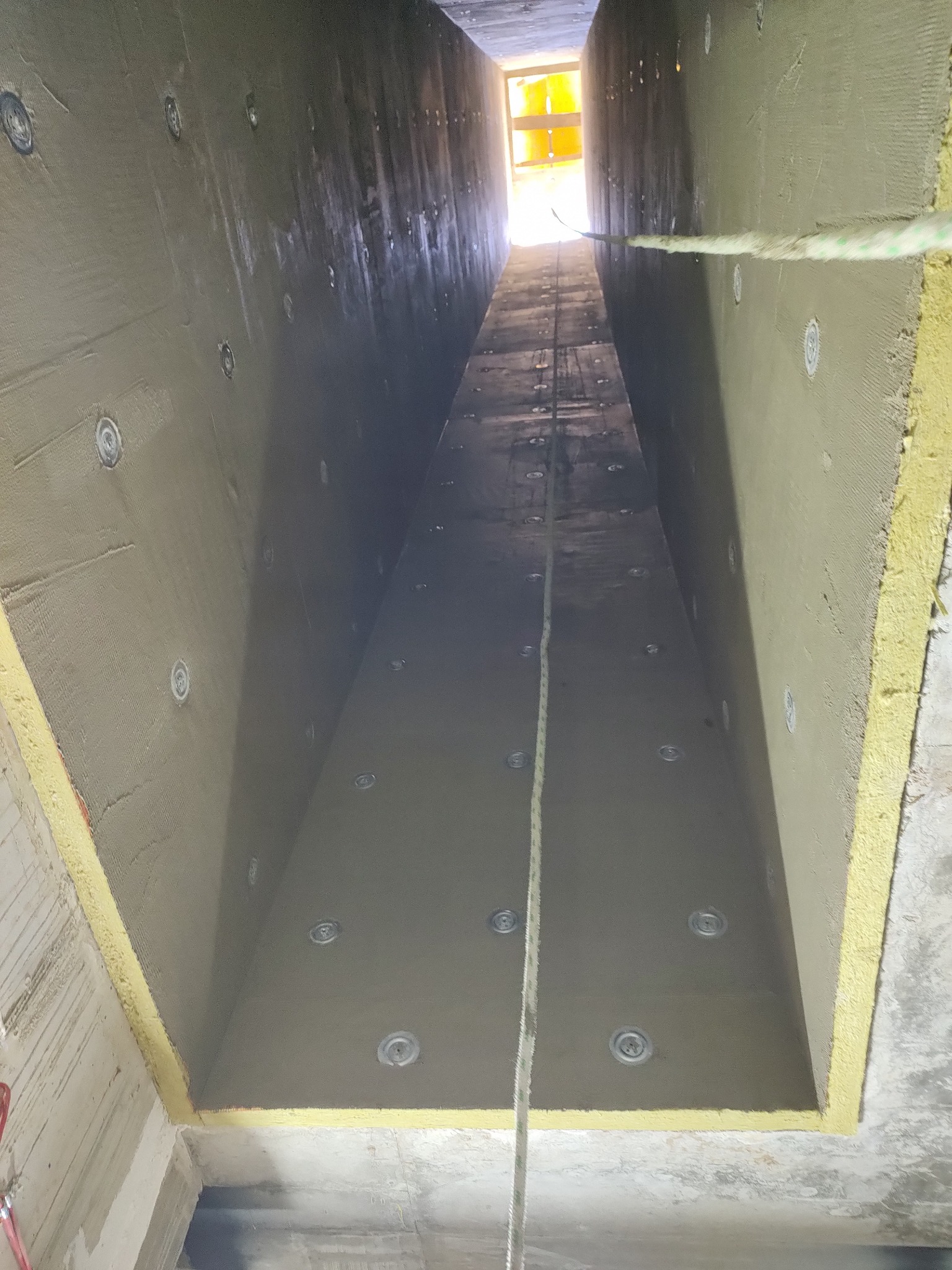 Ocieplony szacht oddymiający systemem CONLIT 150, widok z dołu. Izolacja termiczna i ogniochronna, jasne światło na końcu tunelu. Szpachlowane ściany z widocznymi mocowaniami.