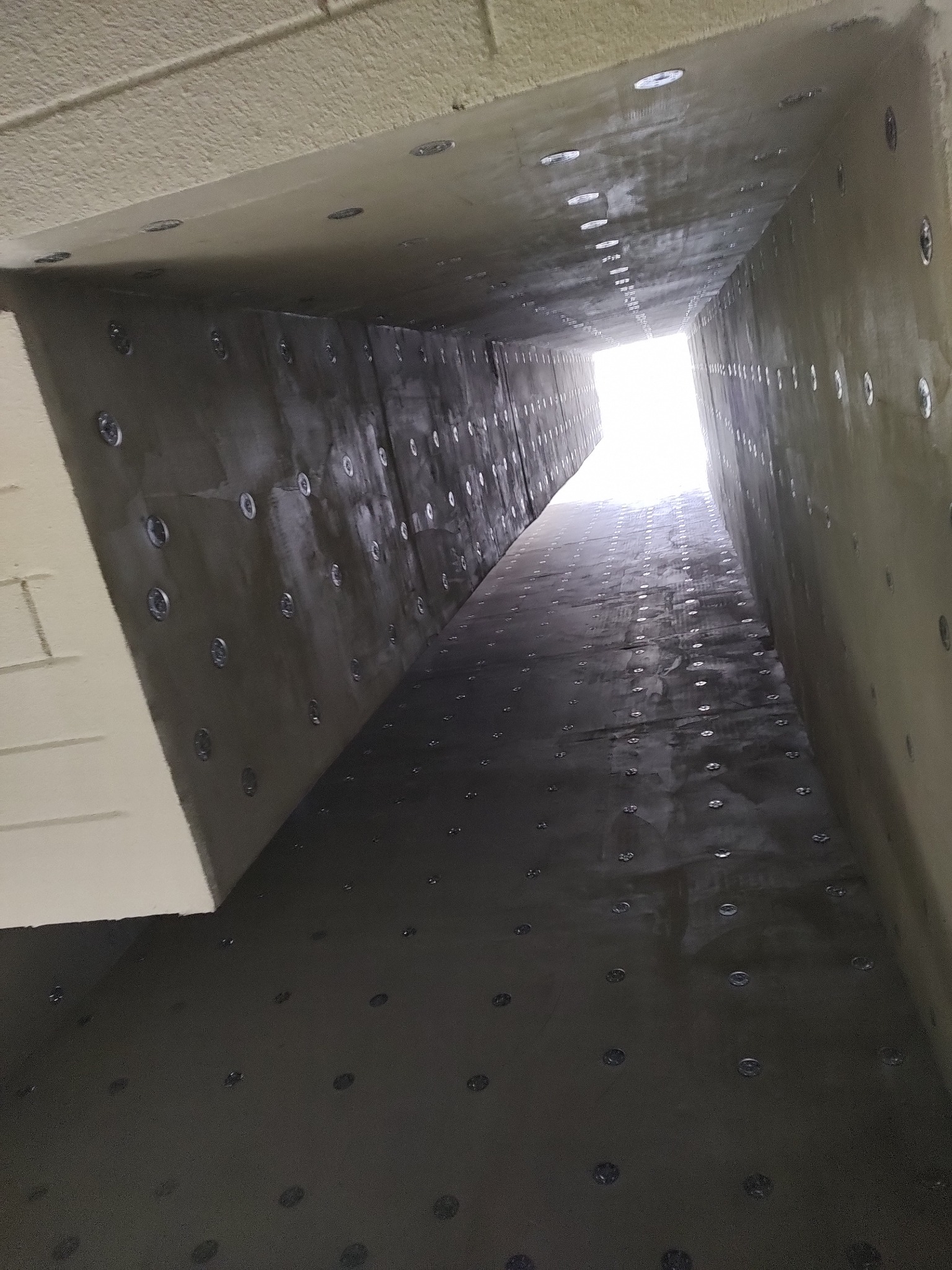 Szacht oddymiający po izolacji ogniochronnej i termicznej systemem CONLIT 150, widok z dołu. Szare ściany z równomiernie rozmieszczonymi mocowaniami.