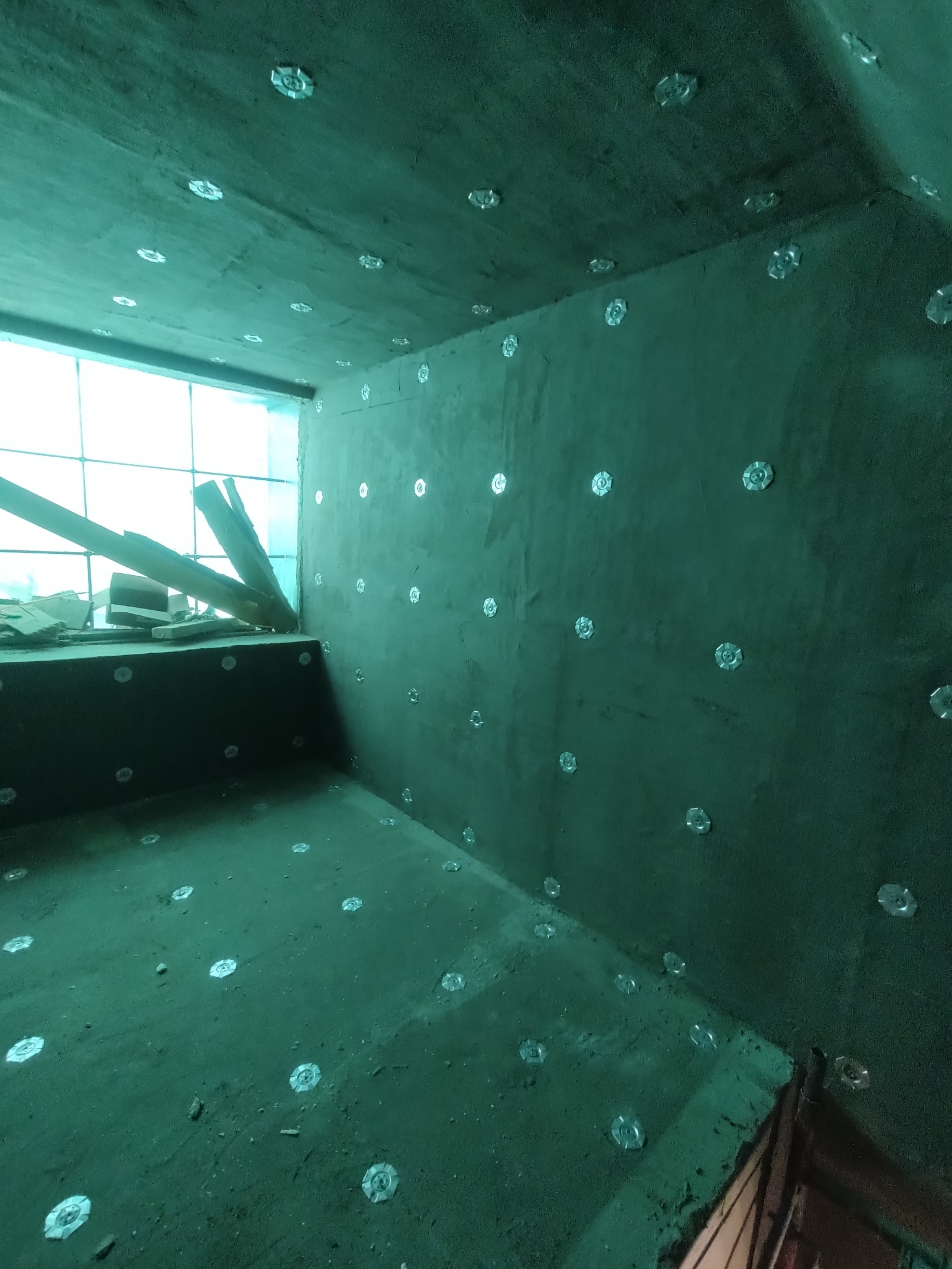 Szacht oddymiający po izolacji ogniochronnej CONLIT 150, widoczne srebrne mocowania na ścianach i suficie. W tle okno z drewnianymi elementami.