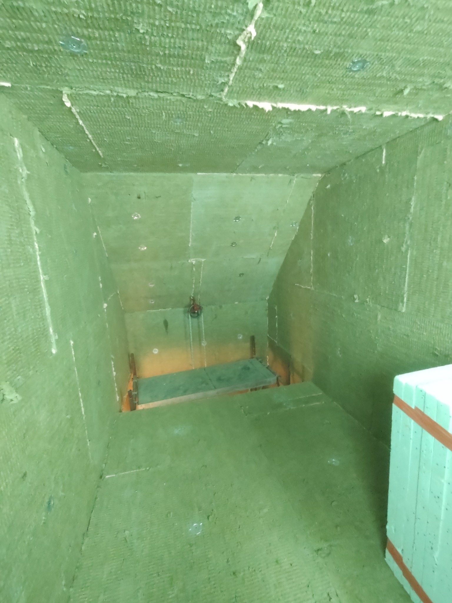 Szacht oddymiający po izolacji ogniochronnej CONLIT 150: zielona wełna mineralna na ścianach, suficie i podłodze, widoczne mocowania i fragment rusztowania.