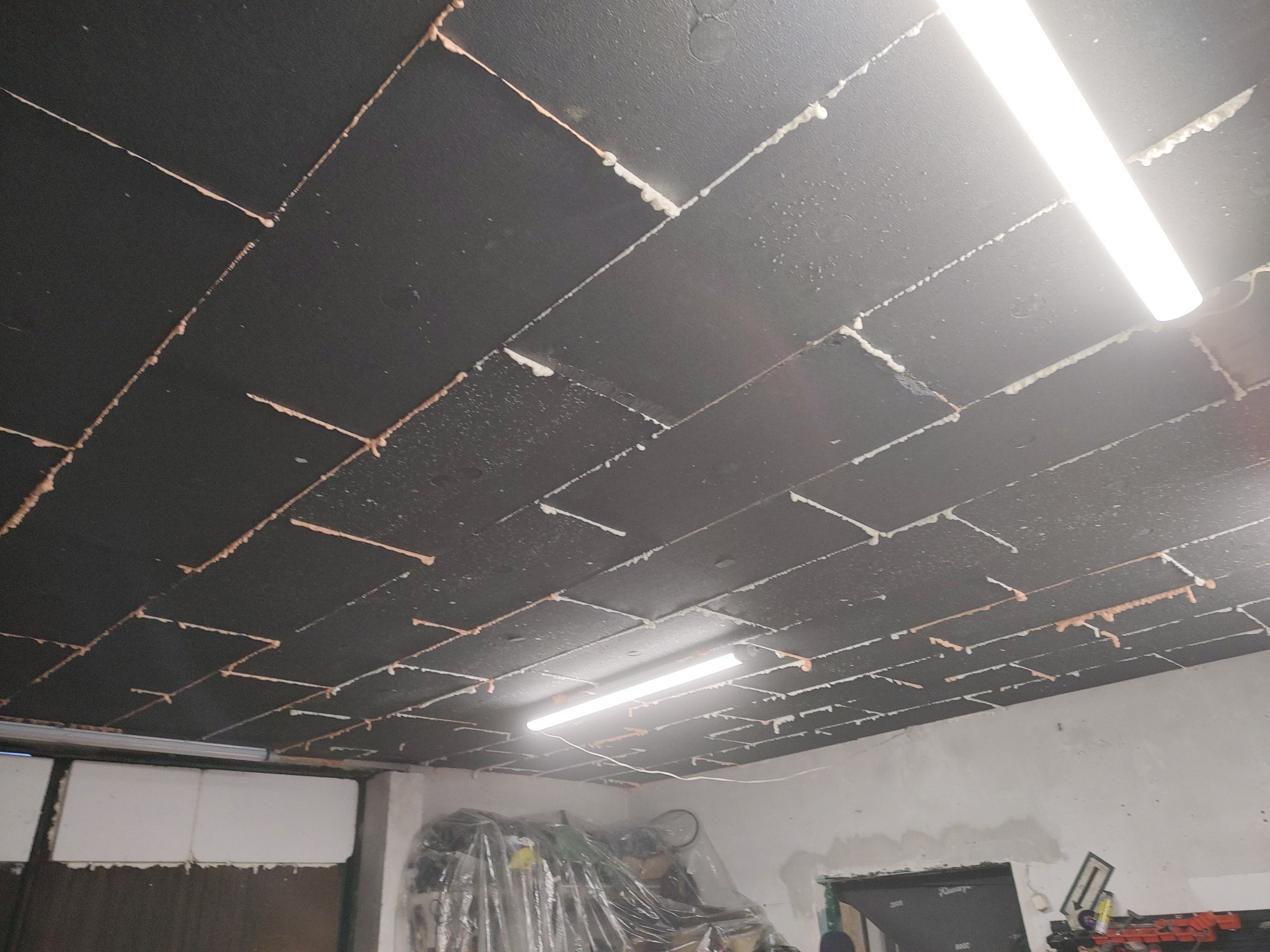 Ocieplony sufit garażu styropianem (15 cm) z zatopioną siatką, widoczne łączenia płyt i dwie lampy jarzeniowe. Całość w surowym, garażowym otoczeniu.