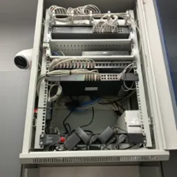 Szafa rack z zamontowanym sprzętem sieciowym: routery, switche, patch panel. Widoczny kabel CCTV. Uporządkowane okablowanie. Montaż w szafie Q-LANTEC.