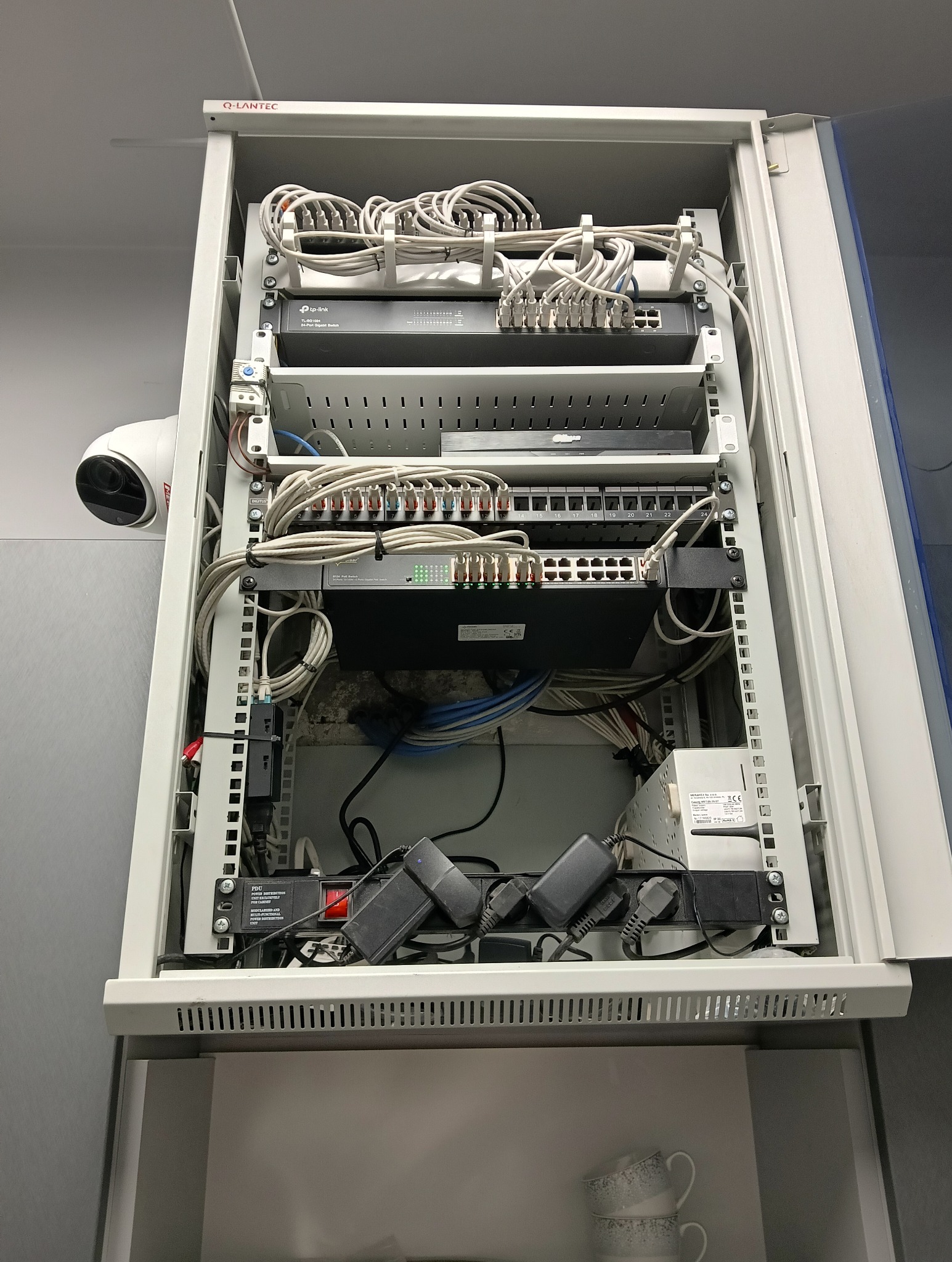 Szafa rack z zamontowanym sprzętem sieciowym: routery, switche, patch panel. Widoczny kabel CCTV. Uporządkowane okablowanie. Montaż w szafie Q-LANTEC.