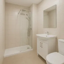 Jasna łazienka po remoncie: kabina prysznicowa ze szklaną ścianką, umywalka z szafką i lustrem, beżowe płytki na ścianach i podłodze, minimalistyczny styl.