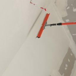 DAWID BOSIAK - Szpachlowanie sufitu pomarańczową szpachelką na teleskopowym kiju. Widoczna zaklejona taśmą instalacja elektryczna i fragmenty niezaszpachlowanej ściany.