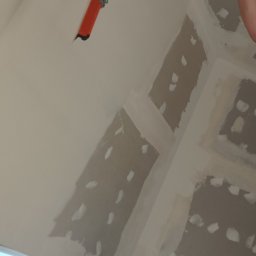 DAWID BOSIAK - Sufit poddasza w trakcie szpachlowania, widoczne łączenia płyt gipsowych, narzędzie do szpachlowania na wysięgniku i fragment drabiny.