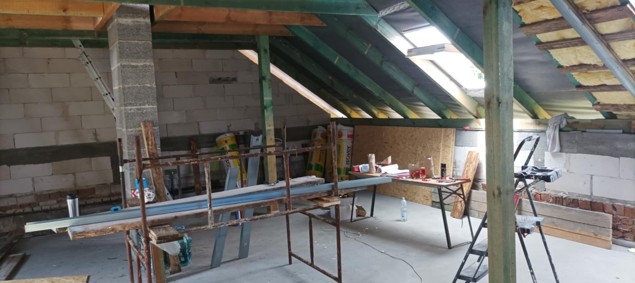 Adaptacja poddasza: widoczne krokwie, ocieplenie, stelaż pod płyty gipsowe, okno dachowe. Prace w toku.