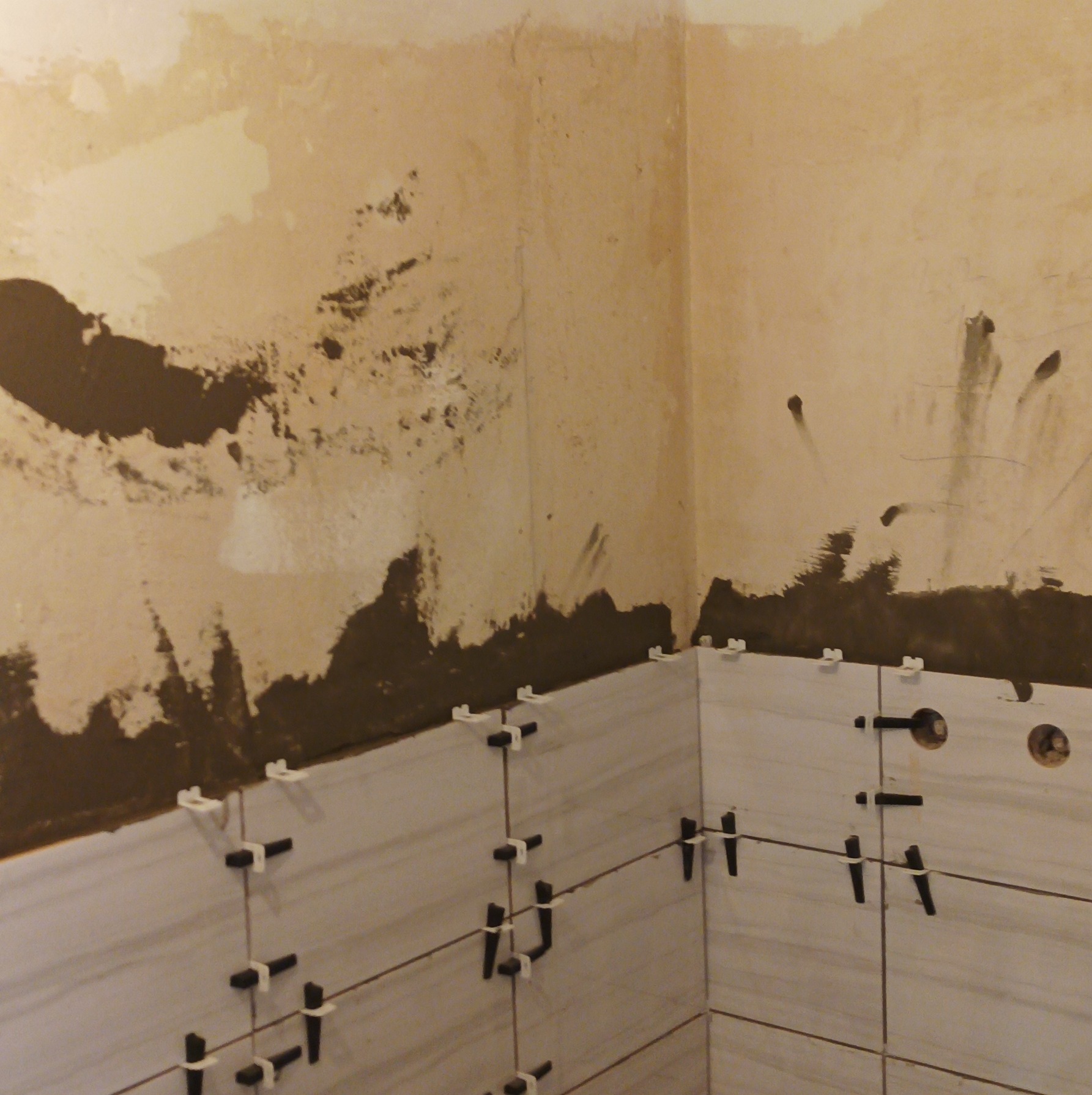 Fragment ściany w trakcie układania płytek z użyciem krzyżyków dystansowych, widoczne ślady zaprawy i przygotowania podłoża.