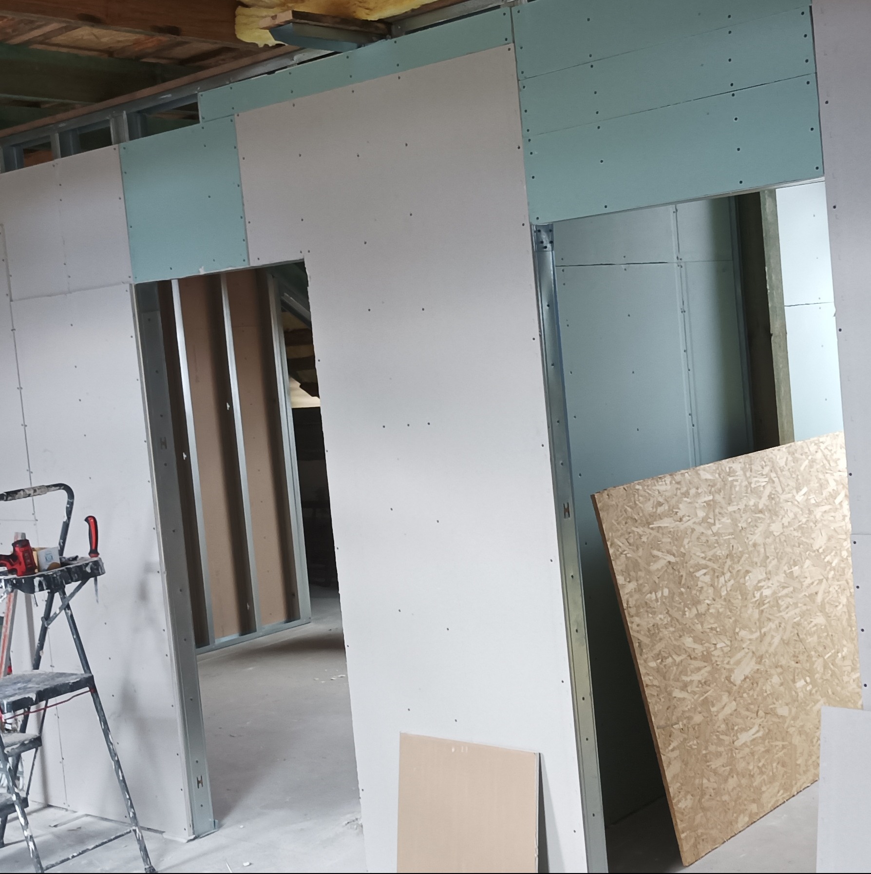 Wnętrze w trakcie montażu ścian działowych z płyt gipsowo-kartonowych na metalowym stelażu. Widoczne otwory drzwiowe i fragment drabiny malarskiej.