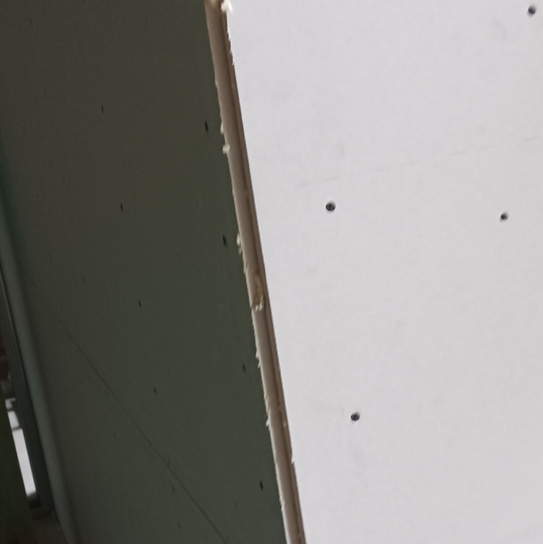 Fragment ściany z płyt karton-gips, widoczne łączenia płyt wypełnione pianką montażową, przygotowane do dalszej obróbki, dziury po wkrętach.