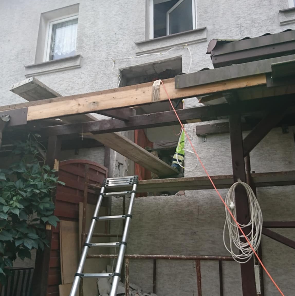 Demontaż fragmentu ściany zewnętrznej budynku, widoczne drewniane elementy konstrukcyjne i drabina, przygotowania do prac budowlanych.