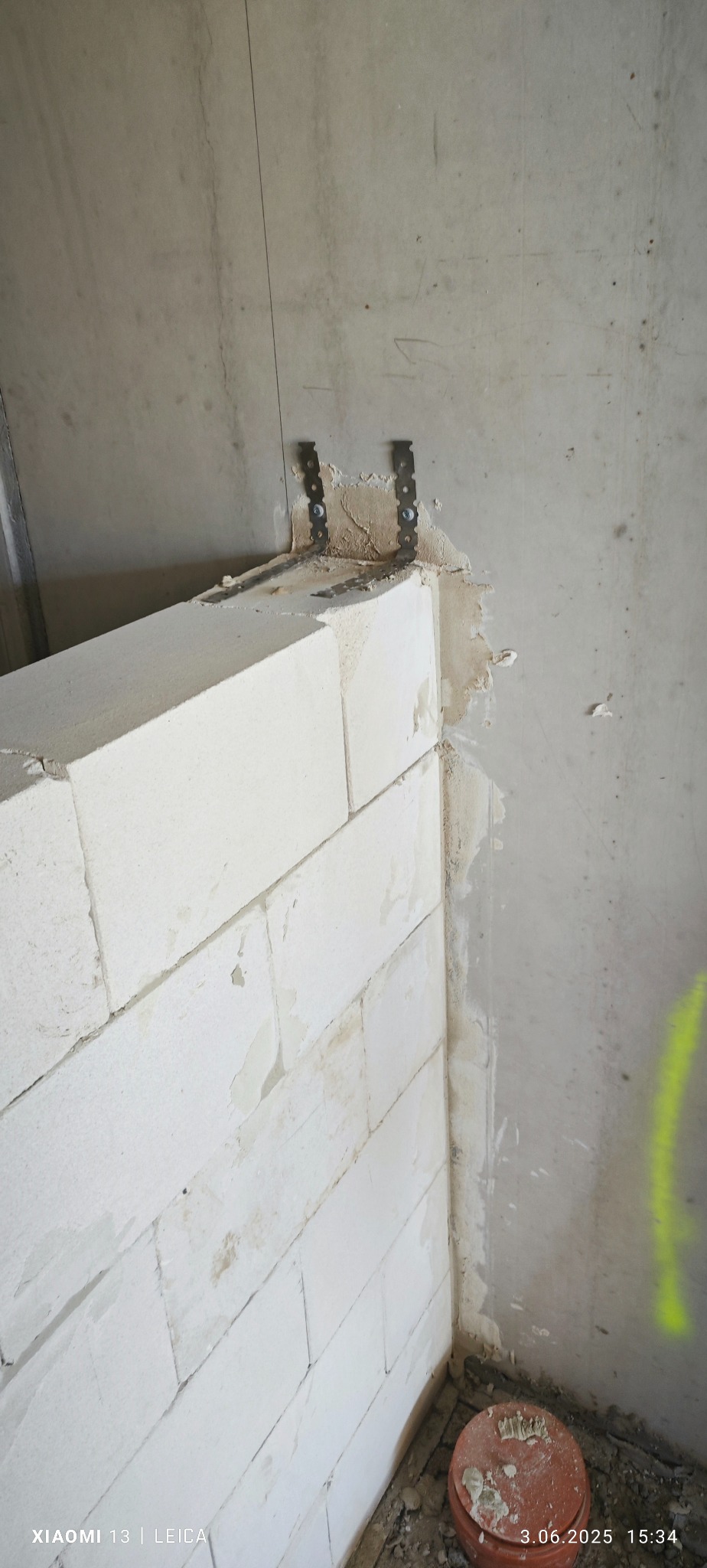 Ściana działowa z betonu komórkowego Ytong, mocowana do ściany za pomocą metalowych łączników. Widoczne zaprawy i niedoskonałości. Etap prac murarskich.