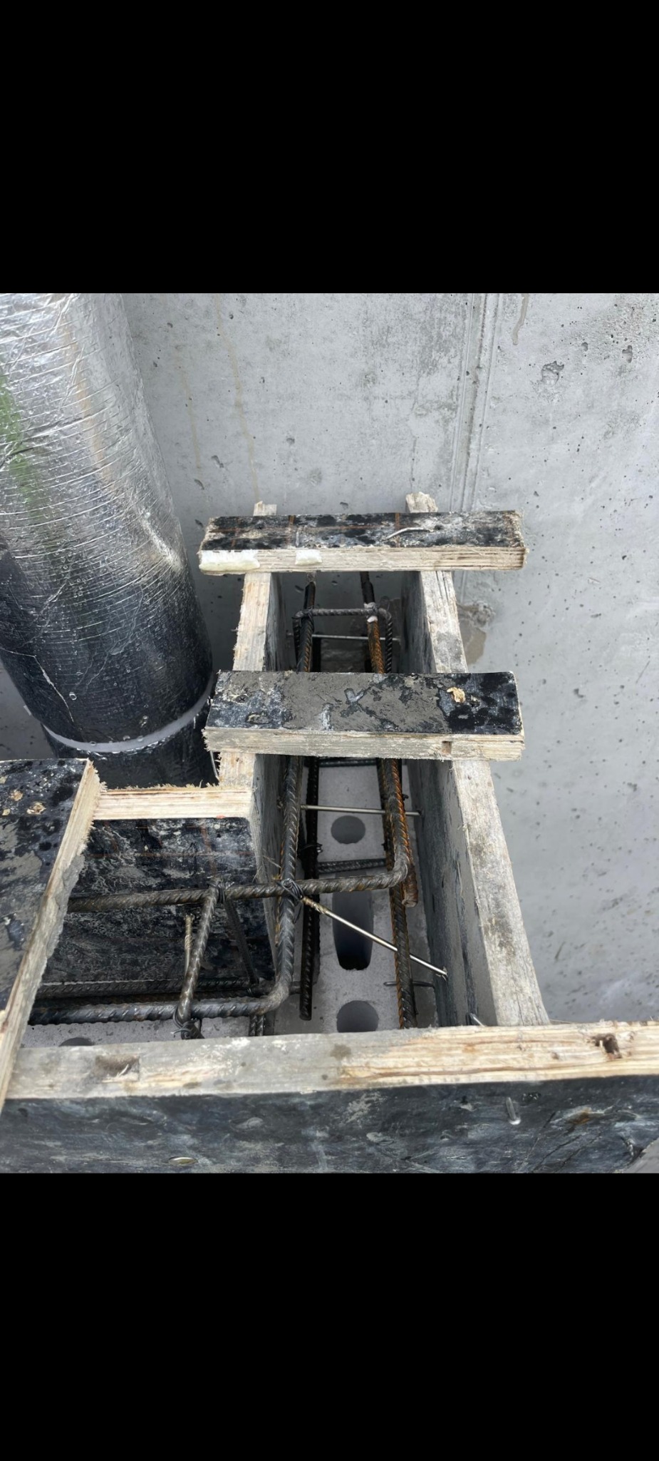 Zbrojenie w szalunku z betonu komórkowego, widok z góry. Element konstrukcyjny w trakcie budowy, z widoczną rurą w tle.