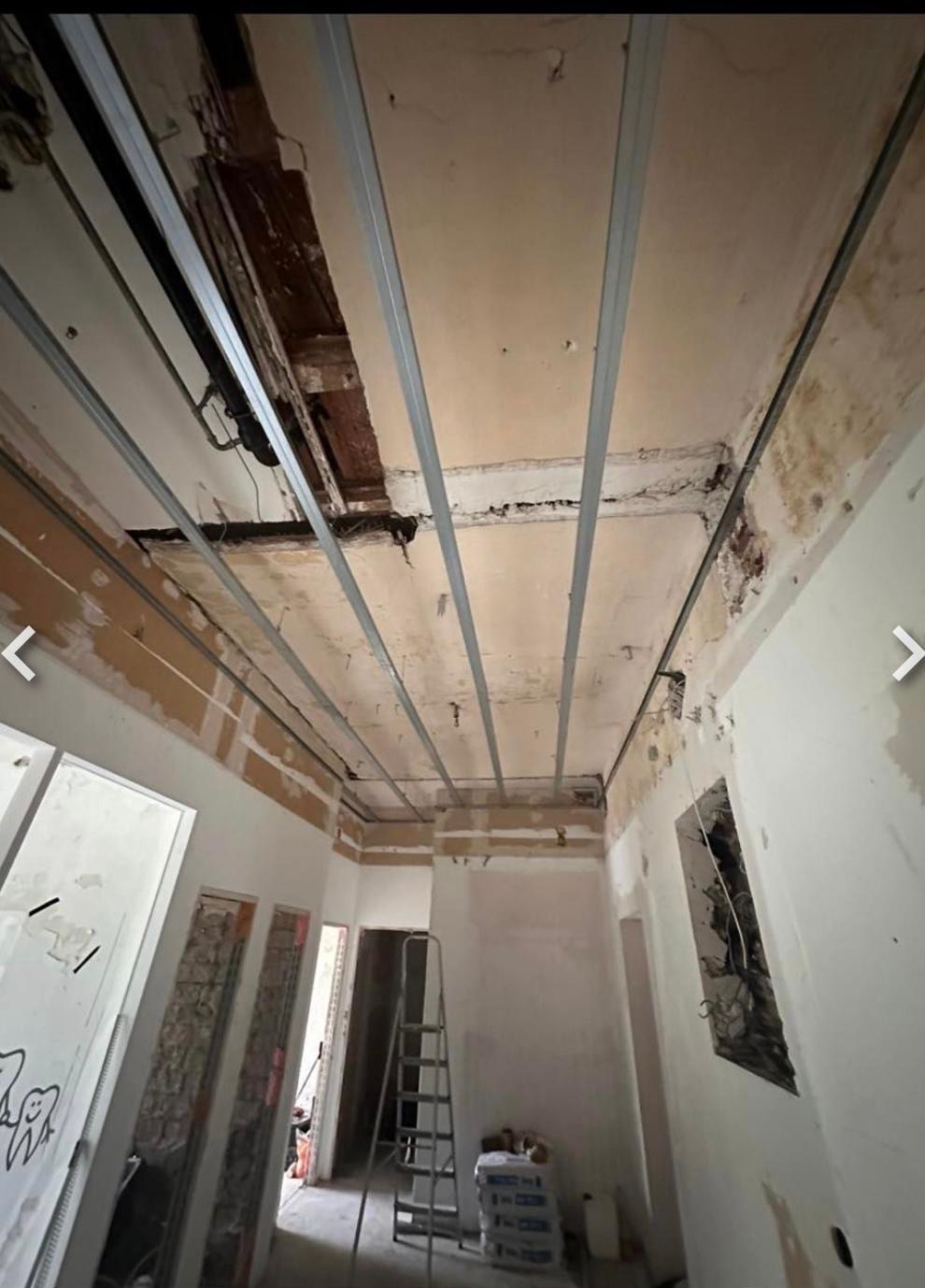 Wnętrze w trakcie remontu: widoczne profile sufitowe, ściany przygotowane do wykończenia, drabina i worki z materiałami budowlanymi. Widok z dołu na sufit.