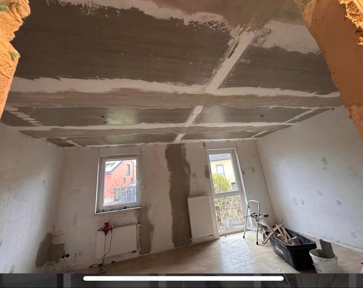 Pokój w trakcie szpachlowania sufitu płytami karton-gips, widoczne narzędzia i drabina. Prace remontowe w jasnym wnętrzu z oknami i grzejnikami.