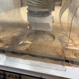 BOGUSŁAW STRYJAK ARTWOOD PRACOWNIA - Obróbka drewna na frezarce CNC z osłoną. Widoczne wióry i fragment obrabianego elementu. Ujęcie z bliska, ukazujące detale procesu.