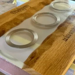 Deska z drewna dębowego z żywicą epoksydową, wtopione metalowe obręcze i wygrawerowane napisy. Blat na etapie wykończenia, zabezpieczony taśmą malarską.