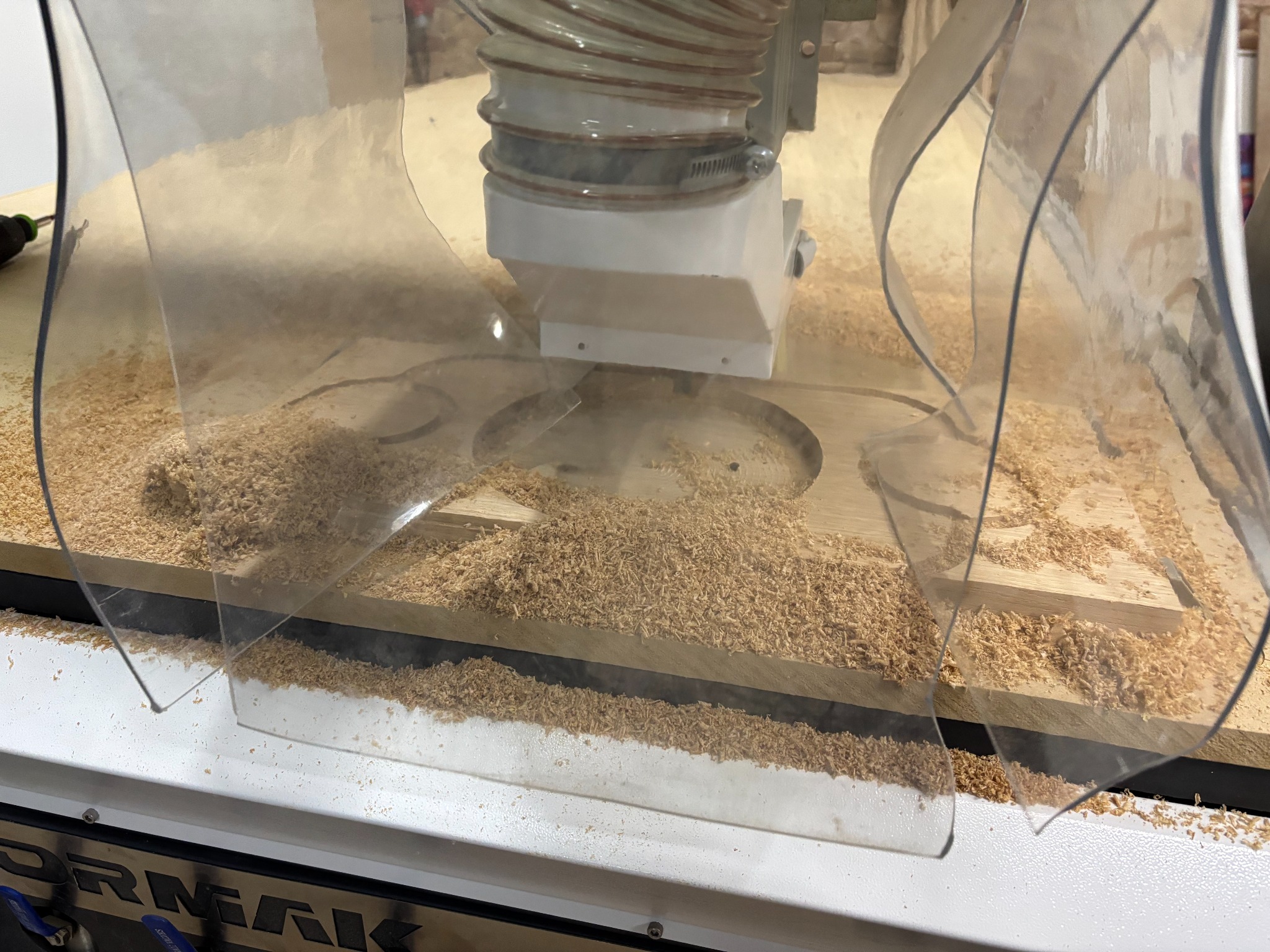 Obróbka drewna na frezarce CNC z osłoną. Widoczne wióry i fragment obrabianego elementu. Ujęcie z bliska, ukazujące detale procesu.