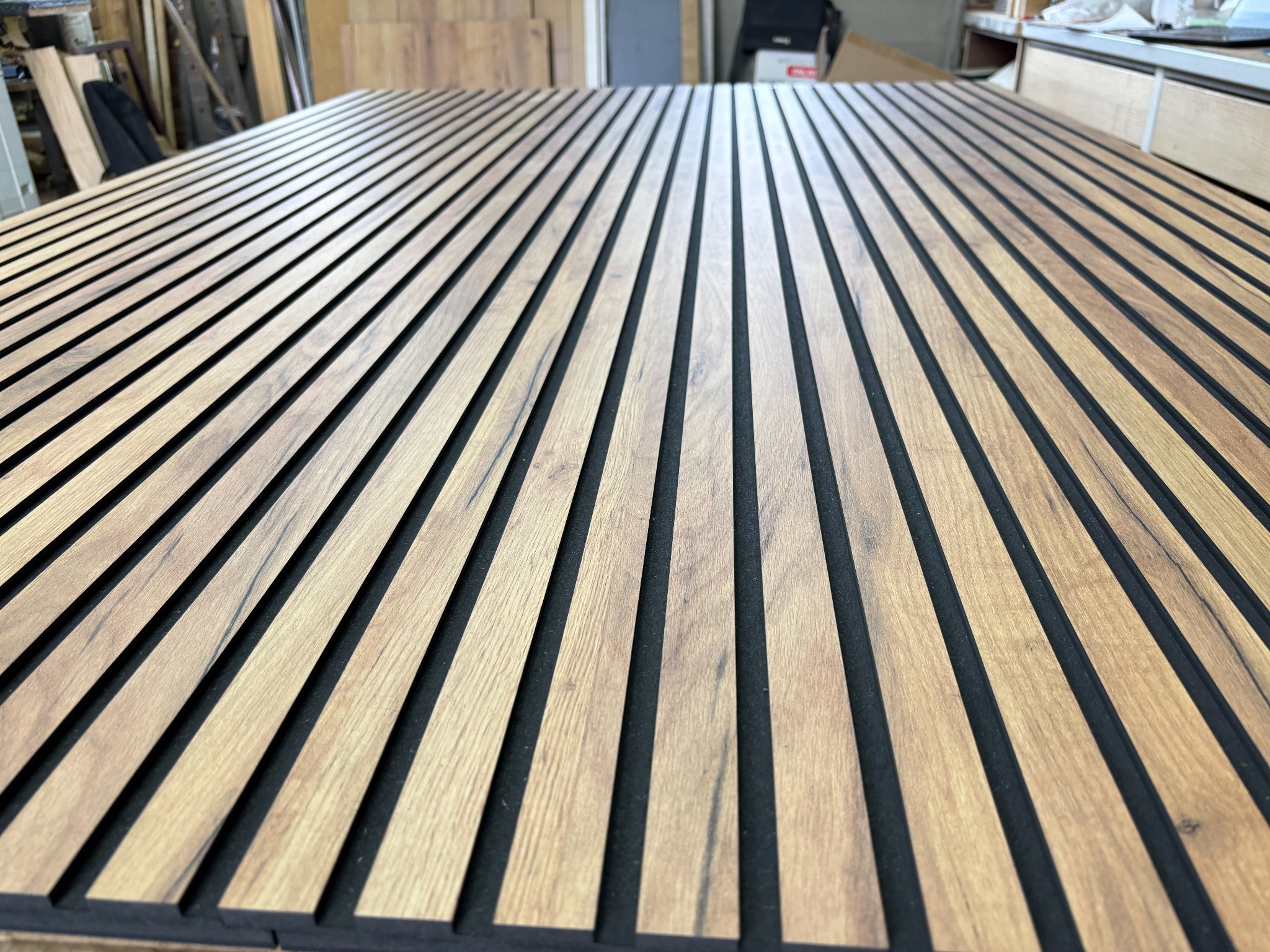 Panel akustyczny z drewnianymi lamelami w Odolanowie. Dekoracyjny element wykończeniowy z wyraźnym rysunkiem drewna i czarnym filcem w tle, ułożony na płasko.