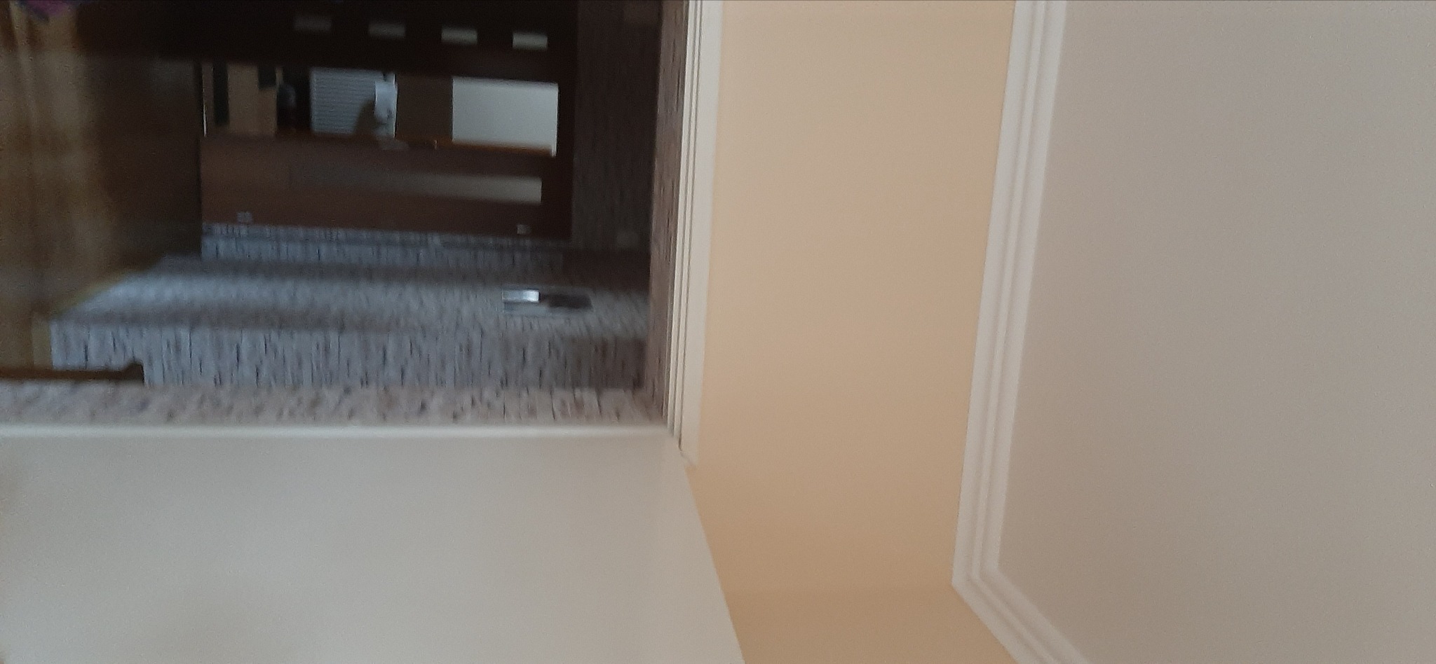 Wykończone wnętrze w Radostowicach: kremowe ściany z dekoracyjnymi listwami, widok na fragment kuchni z szarą mozaiką. Estetyczne detale.