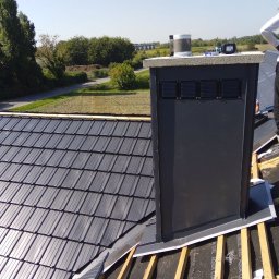 Zarko sp. z o.o. - Ciemnoszara dachówka ceramiczna na połaci dachu w trakcie montażu, widoczny komin wentylacyjny i elementy konstrukcji drewnianej. Słoneczny dzień.