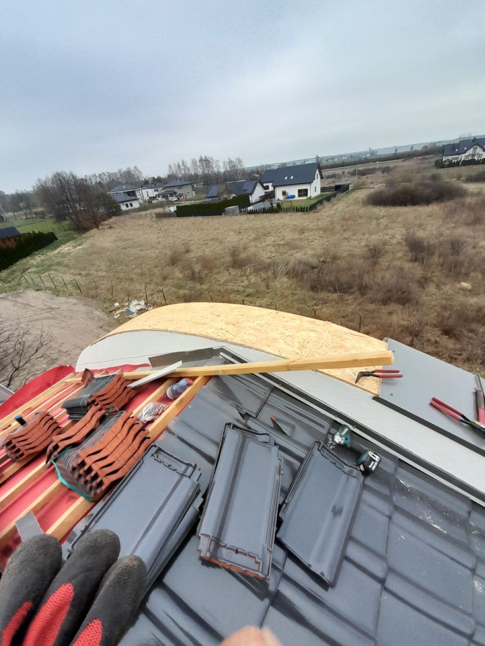 Układanie dachówki ceramicznej na dachu domu jednorodzinnego, widok z góry na częściowo pokryty dach z narzędziami i elementami konstrukcyjnymi.