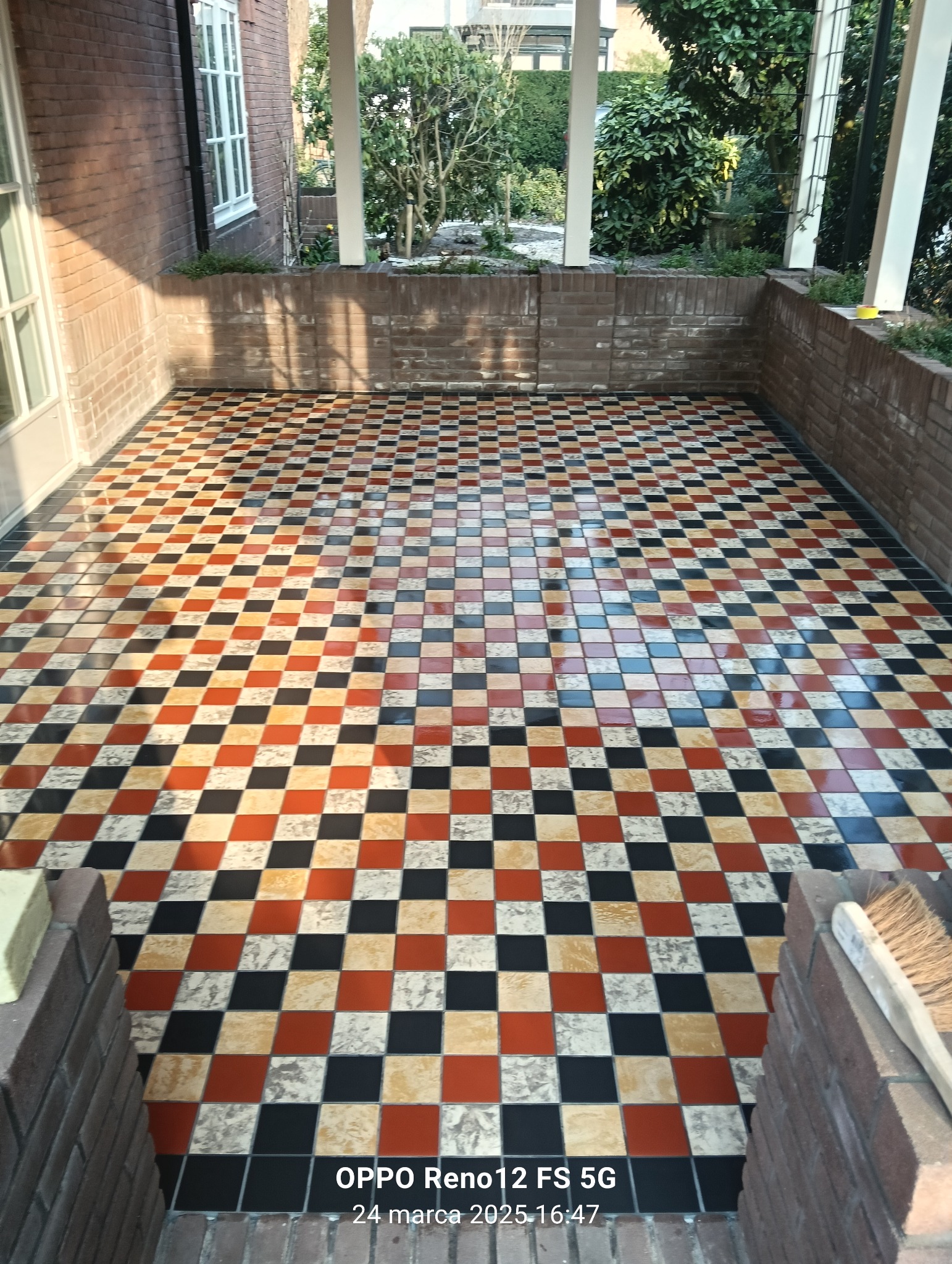 Balkon z nową, błyszczącą posadzką z płytek w szachownicę (czarny, kremowy, pomarańczowy). Widok na zewnątrz przez białe kolumny.