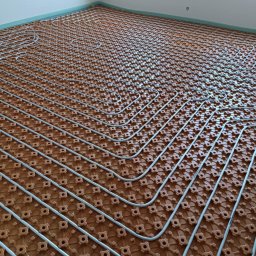 Remont4You - Instalacja ogrzewania podłogowego: rury ułożone na brązowej macie z wypustkami, widok z góry. Etap prac przed wylaniem posadzki.