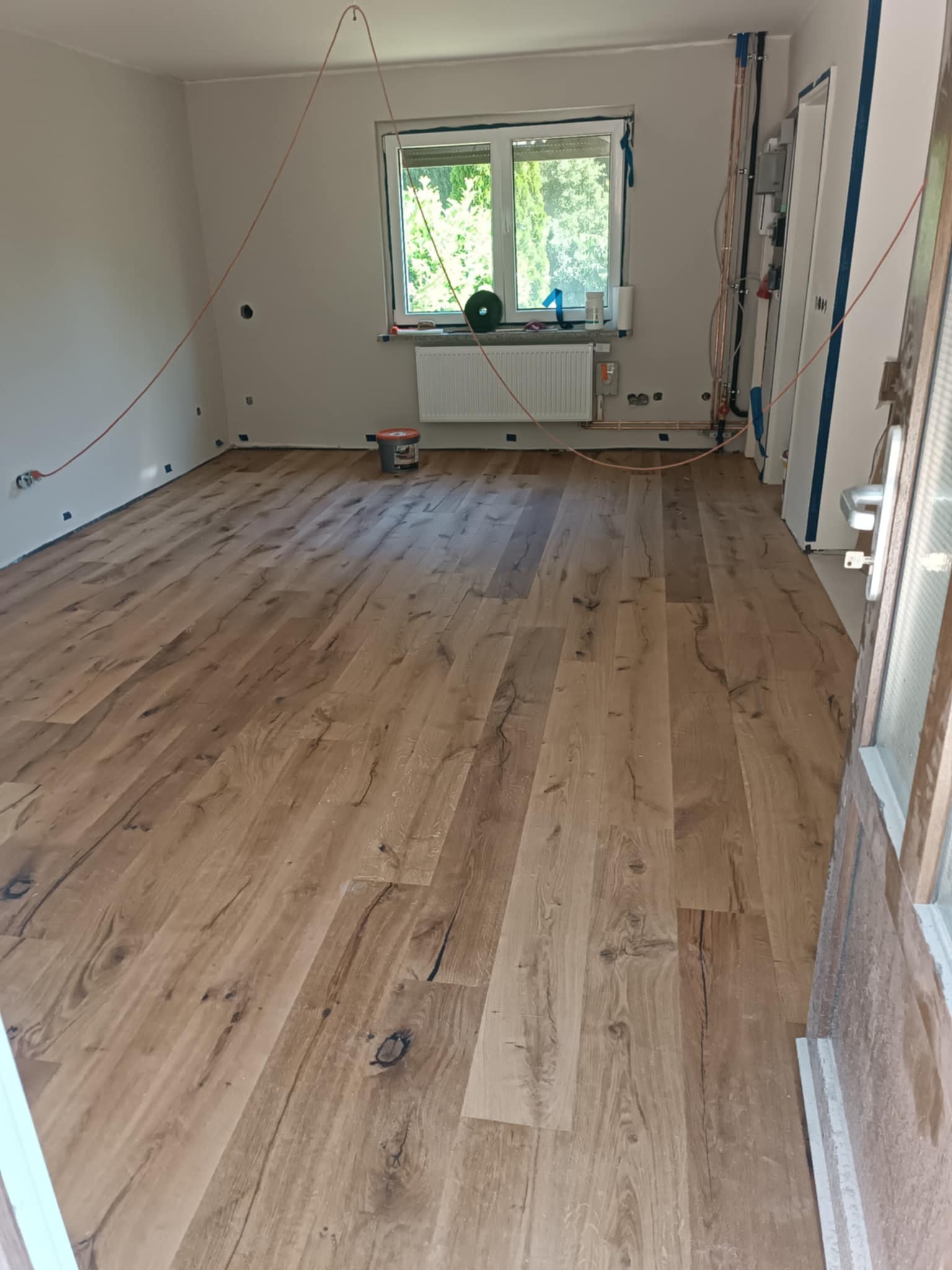 Ukończona podłoga z paneli drewnianych w jasnym wnętrzu. Widoczne przygotowania do dalszych prac wykończeniowych: zabezpieczenia, instalacje.