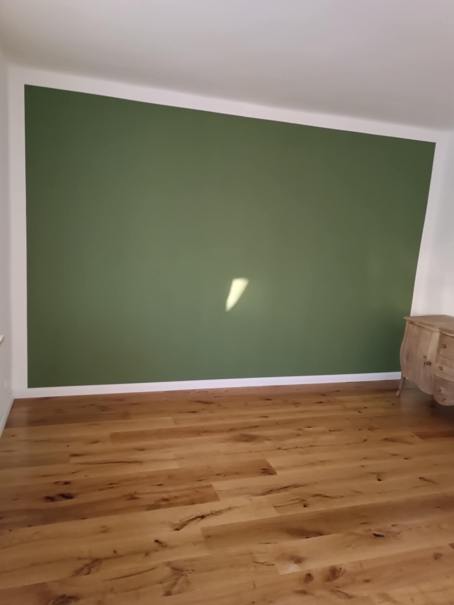 Pomieszczenie po malowaniu ścian na oliwkowy kolor i ułożeniu parkietu. Widoczna komoda. Realizacja w Maszewie.