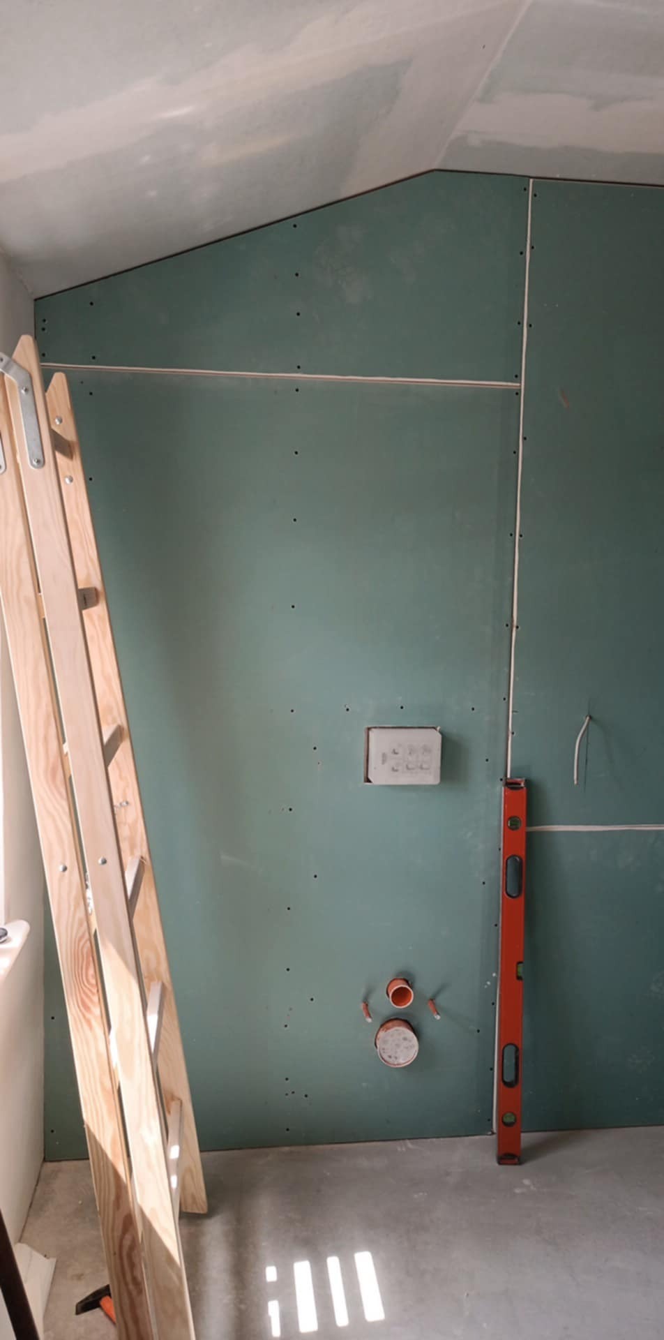 Ściana z płyt karton gips w trakcie montażu, widoczne łączenia, poziomica i drabina. Otwór na instalację elektryczną i sanitarną.