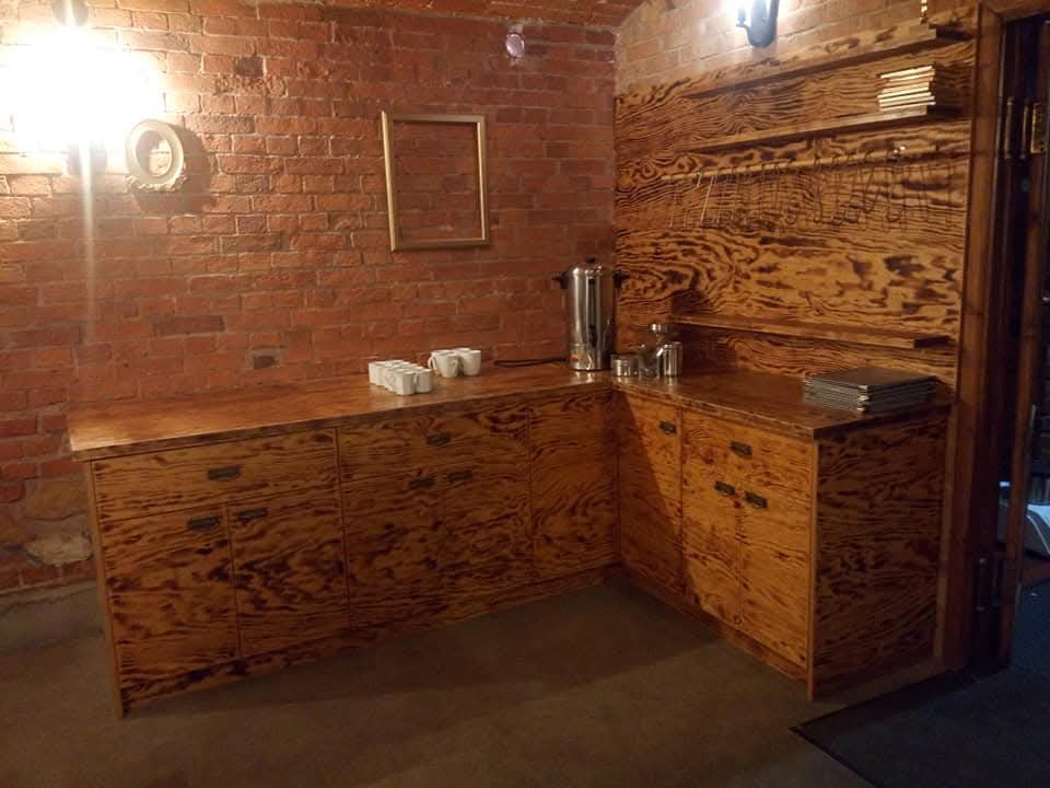 Wyjątkowa zabudowa kuchenna z wzorzystego drewna, z blatem i szafkami w rustykalnym stylu, na tle ceglanej ściany i drewnianej boazerii.