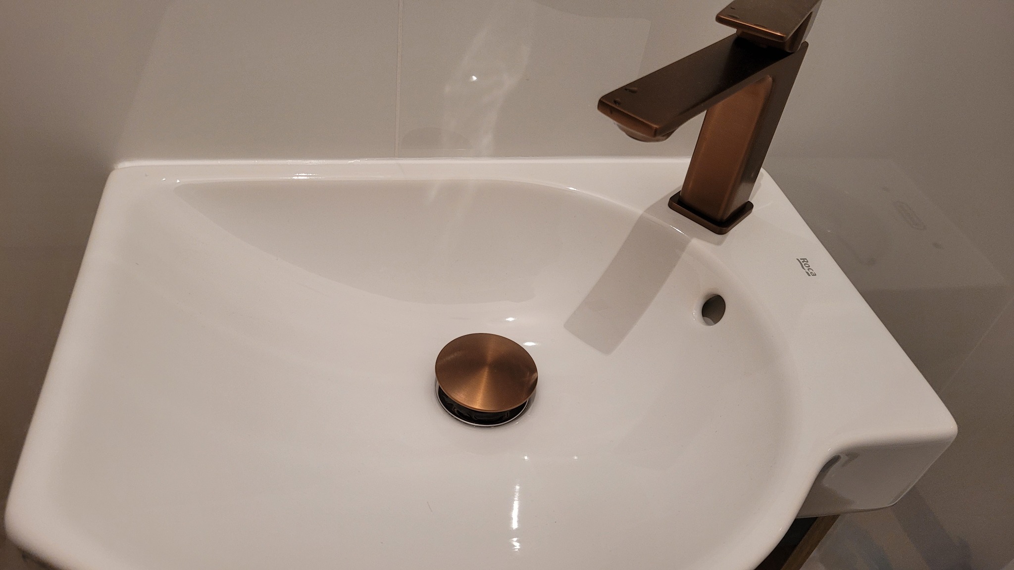 Biała umywalka z brązową armaturą i korkiem. Ujęcie z góry prezentuje minimalistyczny design i nowoczesne wykończenie łazienki, podkreślając detale.