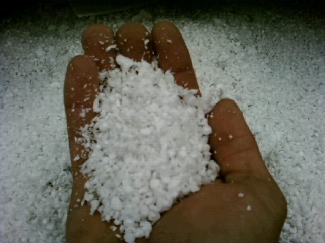 Dłoń trzymająca biały granulat po frezowaniu styropianu na tle rozsypanego materiału.