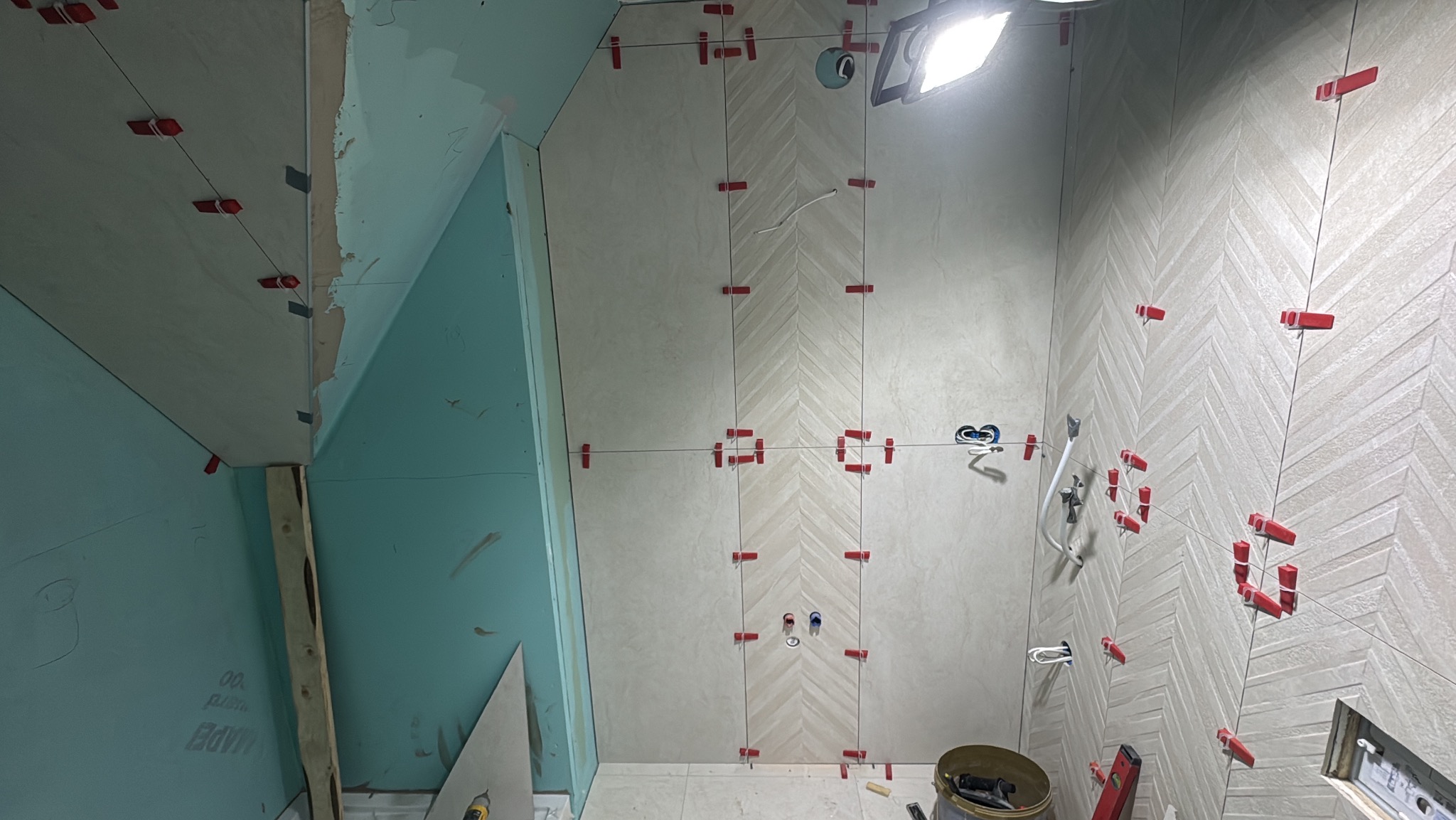 Układanie płytek w jodełkę w łazience, z użyciem klipsów poziomujących. Widoczne przygotowane ściany z płyt kartonowo-gipsowych i narzędzia glazurnicze.