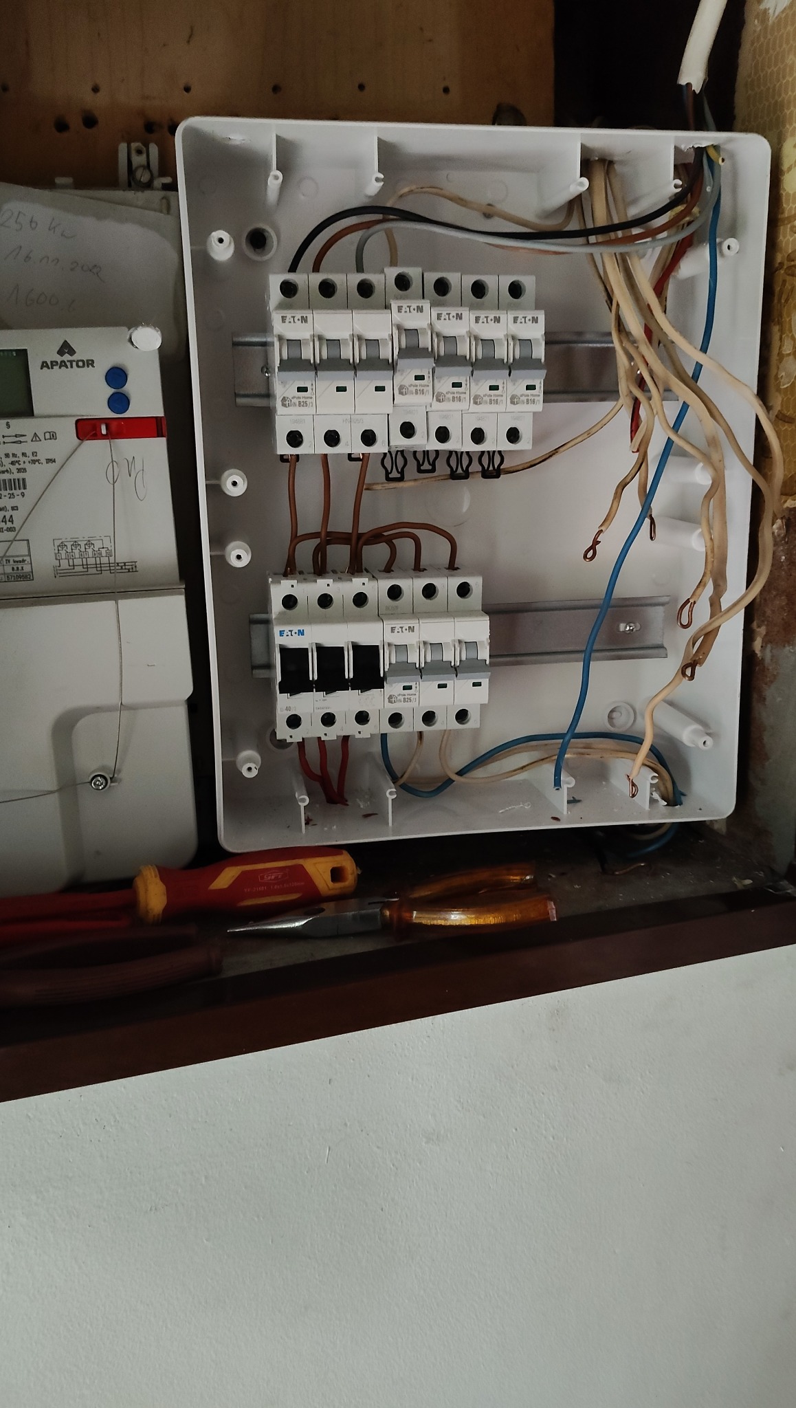 Rozdzielnica elektryczna marki Eaton z zainstalowanymi bezpiecznikami, widoczne przewody i narzędzia. Ujęcie z bliska, ukazujące szczegóły instalacji.