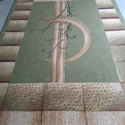 Wyczyszczony, zielony dywan z geometrycznym wzorem i motywem drzewa, leżący na szarej podłodze. Widoczny wąż od odkurzacza w tle po lewej stronie.