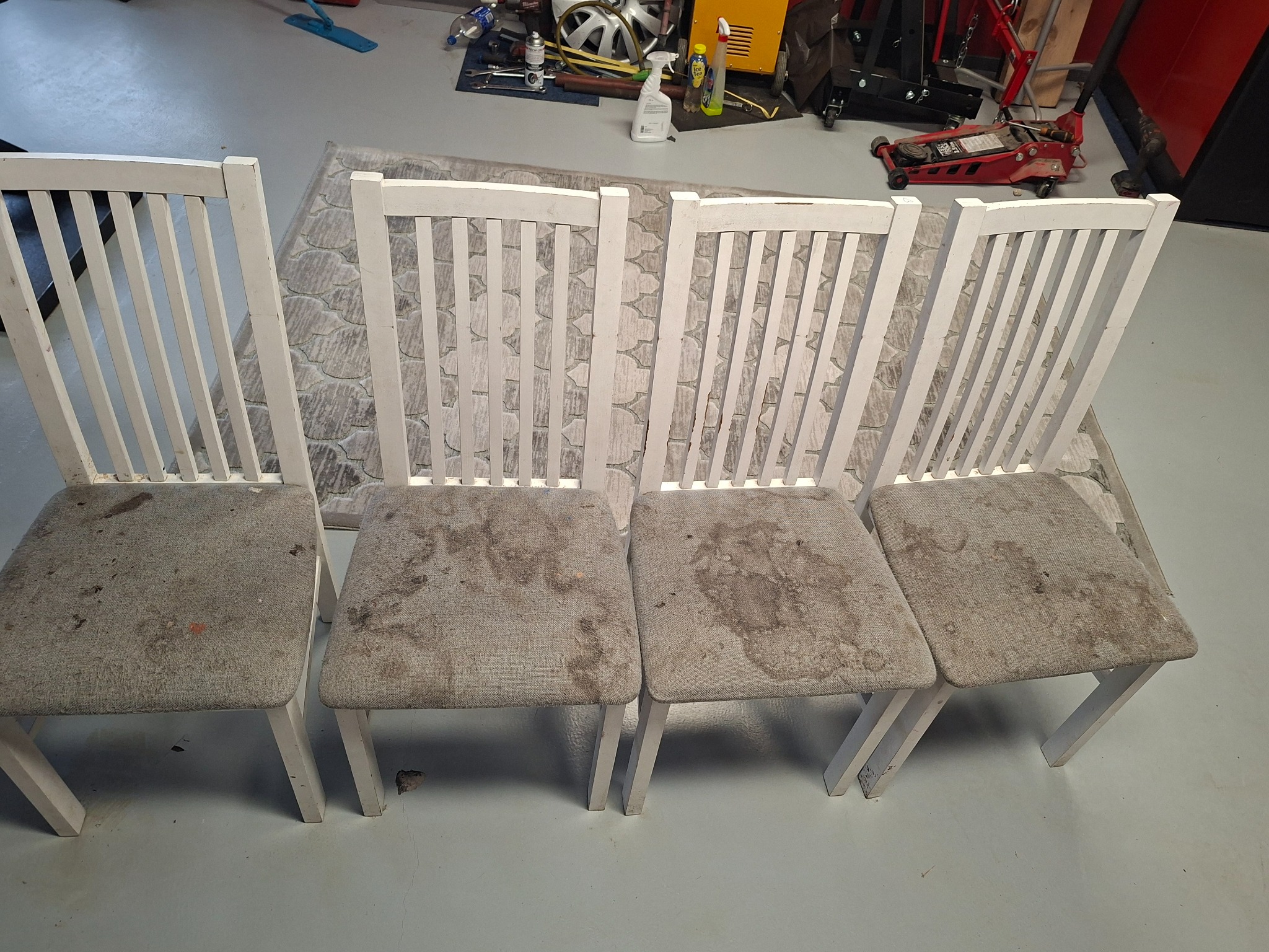 Cztery białe krzesła z szarą tapicerką przed dywanem, widoczne plamy na siedziskach, sugerujące potrzebę czyszczenia tapicerki meblowej.