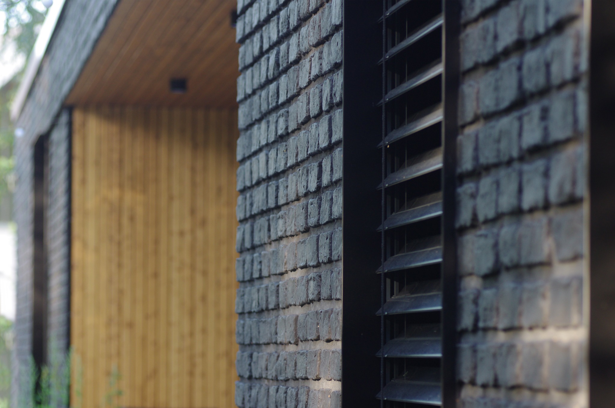 Detale elewacji domu: czarna cegła licówka, drewniana fasada i żaluzje. Elementy architektoniczne w nowoczesnym stylu.