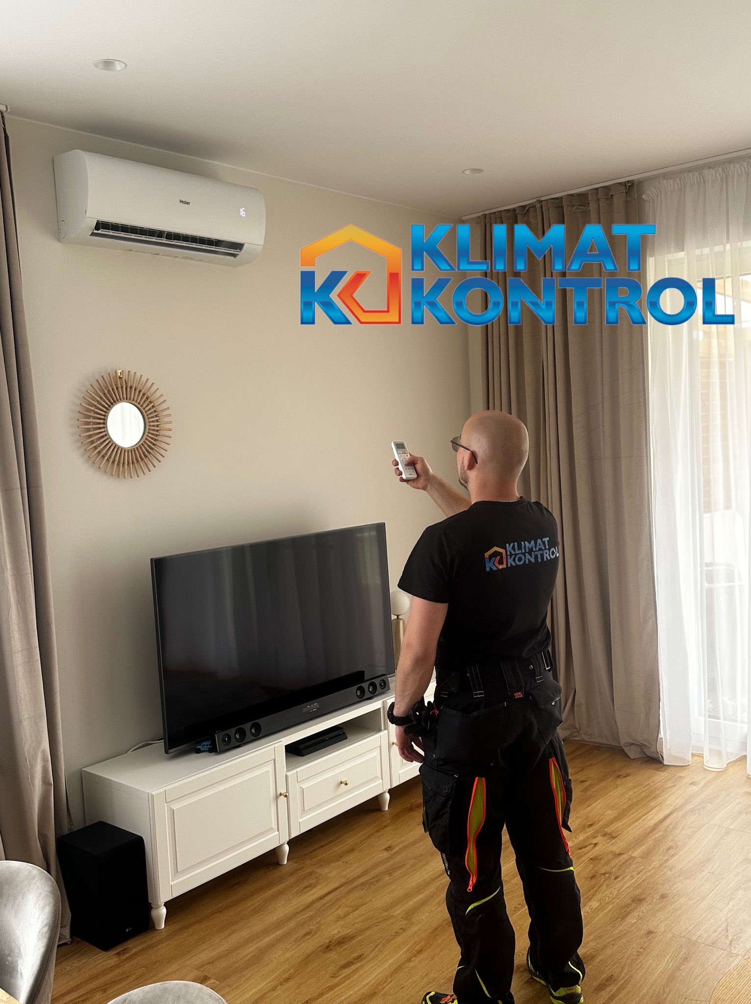 Instalacja klimatyzacji w salonie: monter z pilotem celuje w biały klimatyzator Haier. Widoczne logo firmy na koszulce montera i grafika 'Klimat Kontrol'.
