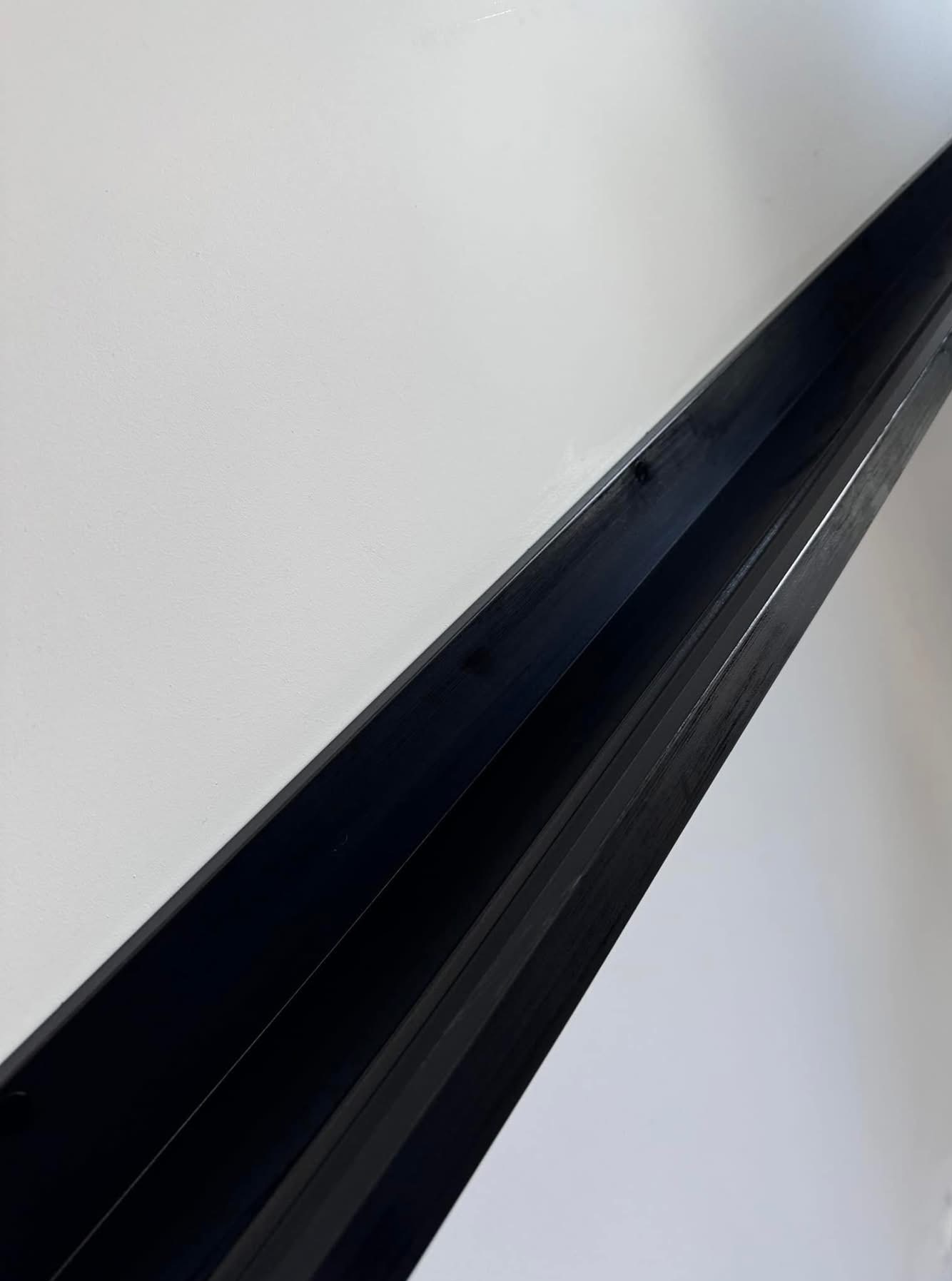 Wnętrze czystej, pomalowanej na biało ściany z zainstalowaną, długą, czarną listwą przypodłogową. Minimalistyczny design, świeżo po montażu.