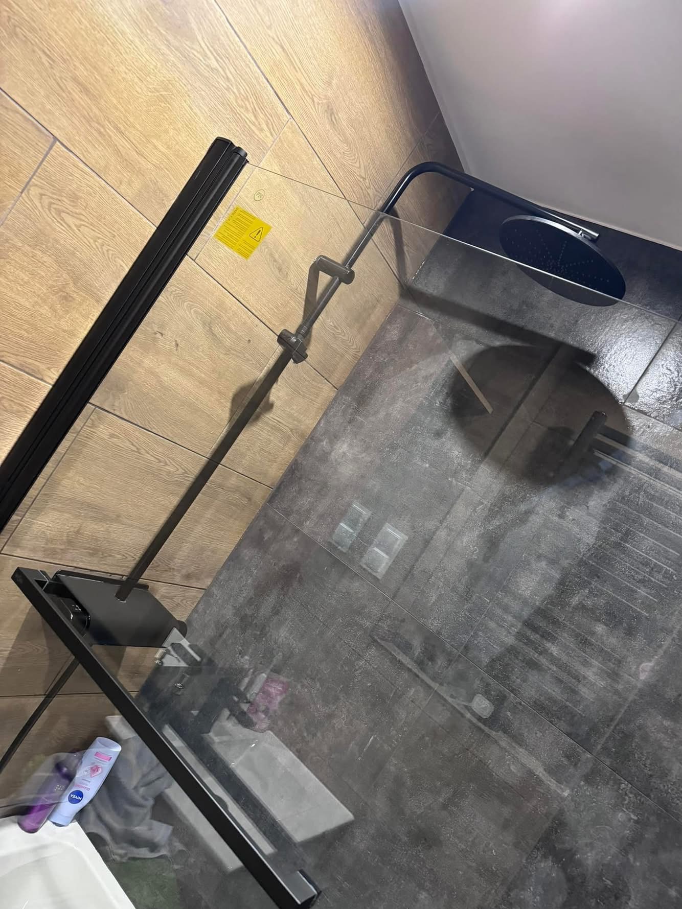 Nowoczesna kabina prysznicowa z czarną armaturą i szklanymi ściankami, widok z góry na czyste płytki podłogowe. Minimalistyczny design łazienki po sprzątaniu.